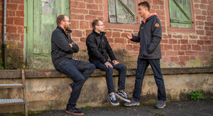 Drei Personen mit MeJeans besprechen sich vor einem rustikalen Gebäude 